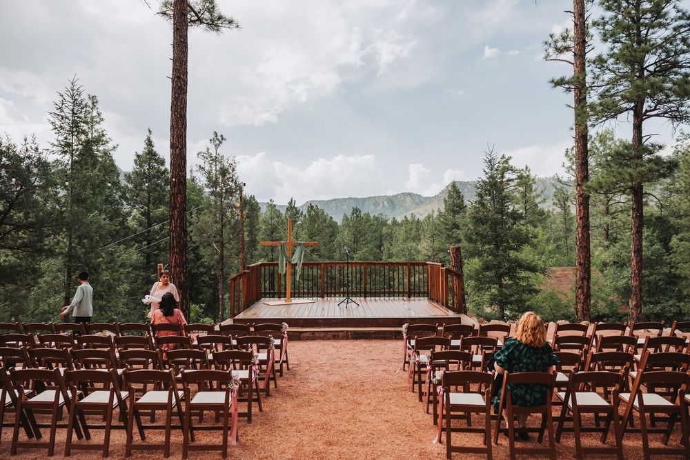 Panoramic view of a mountaintop wedding ceremony setup with wooden chairs arranged in rows on red clay ground.