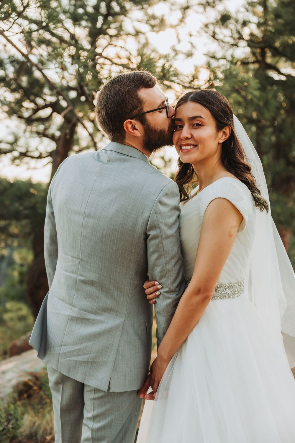 Happy newlywed couple shares intimate moments at a sunny outdoor wedding ceremony with natural greenery backdrop.