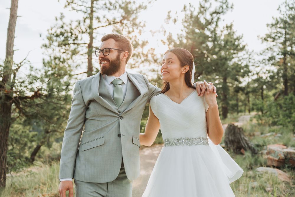 Happy newlyweds share a joyful moment together outdoors in a sunlit forest wearing wedding attire.
