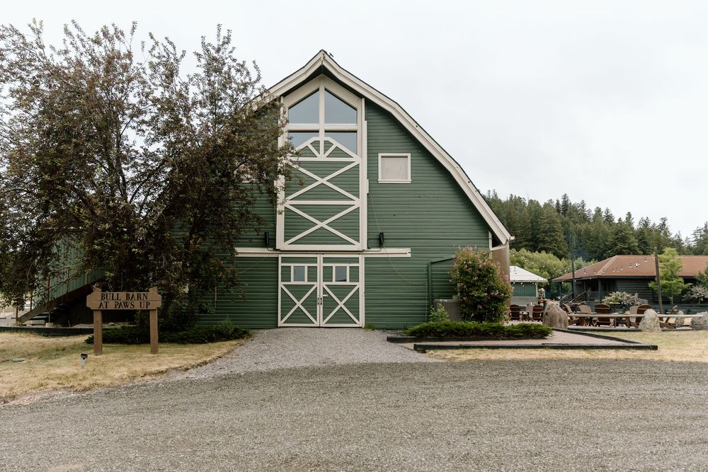 Large green barn-style building with white trim and gravel driveway in rural setting.