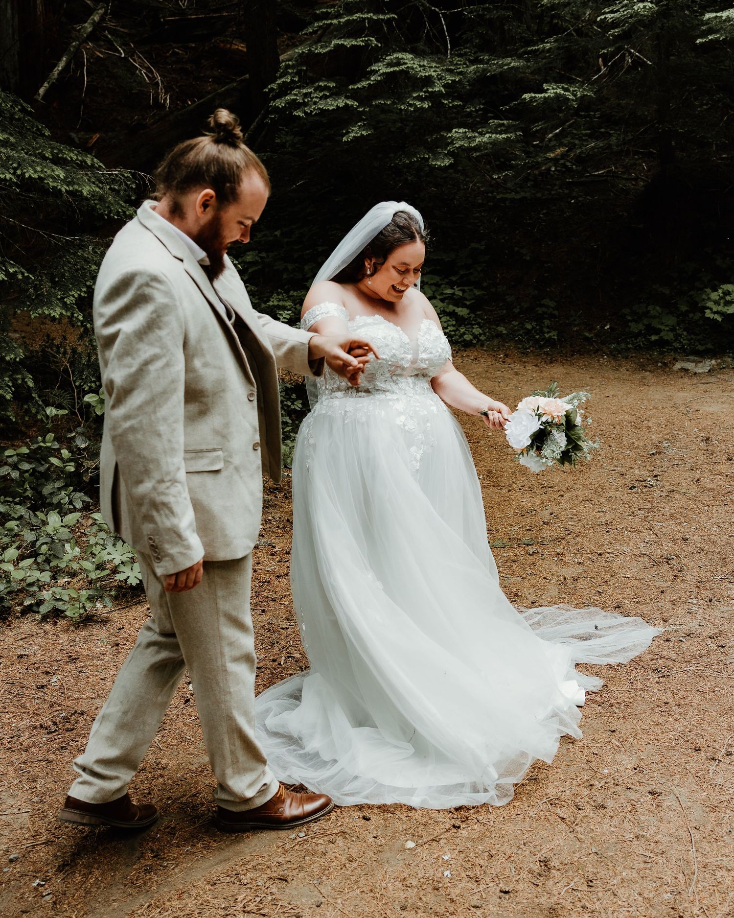 Wedding couple walking together on forest path in elegant attire.
