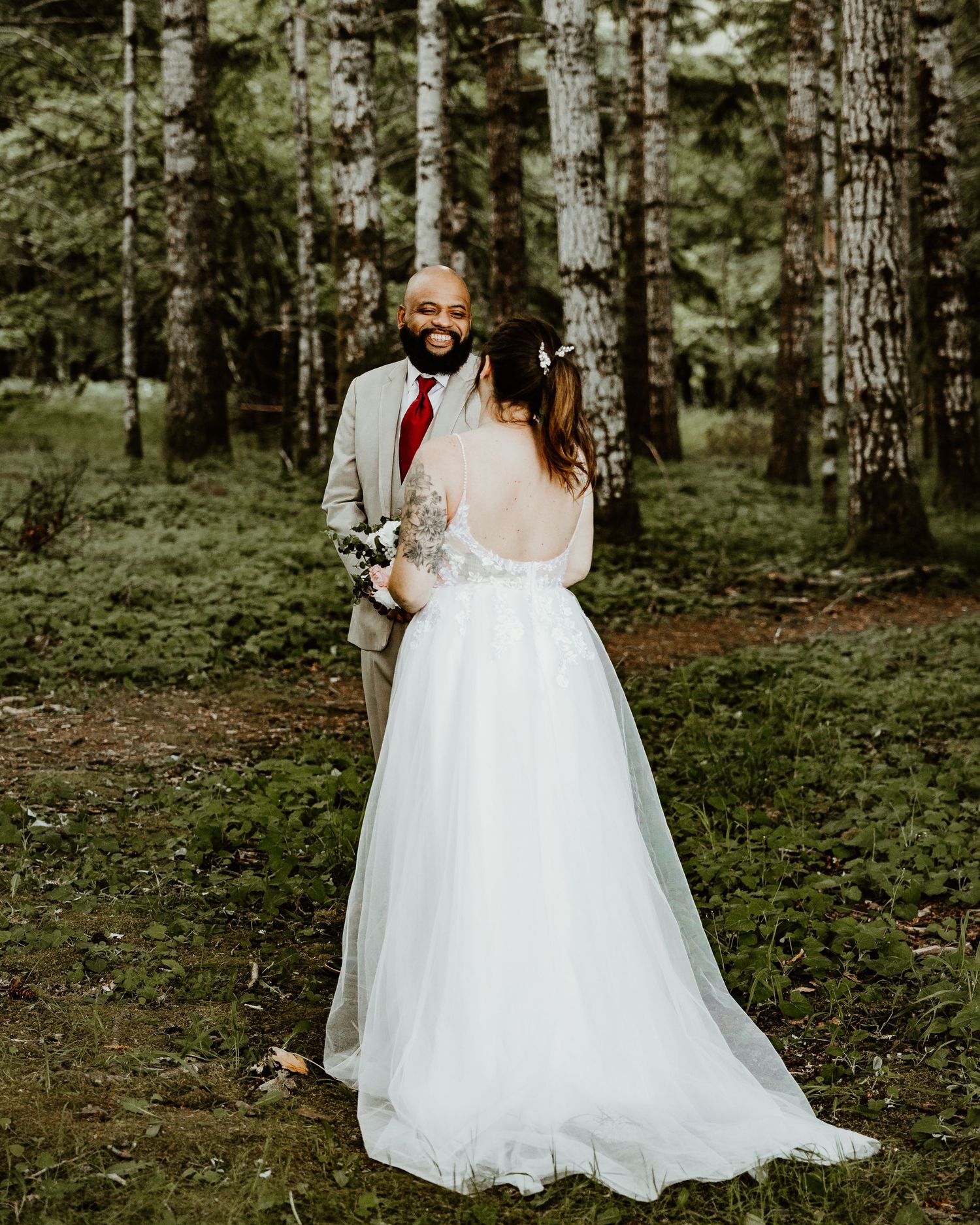An elegant wedding couple stands together in a peaceful forest setting surrounded by tall pine trees. what is a First look