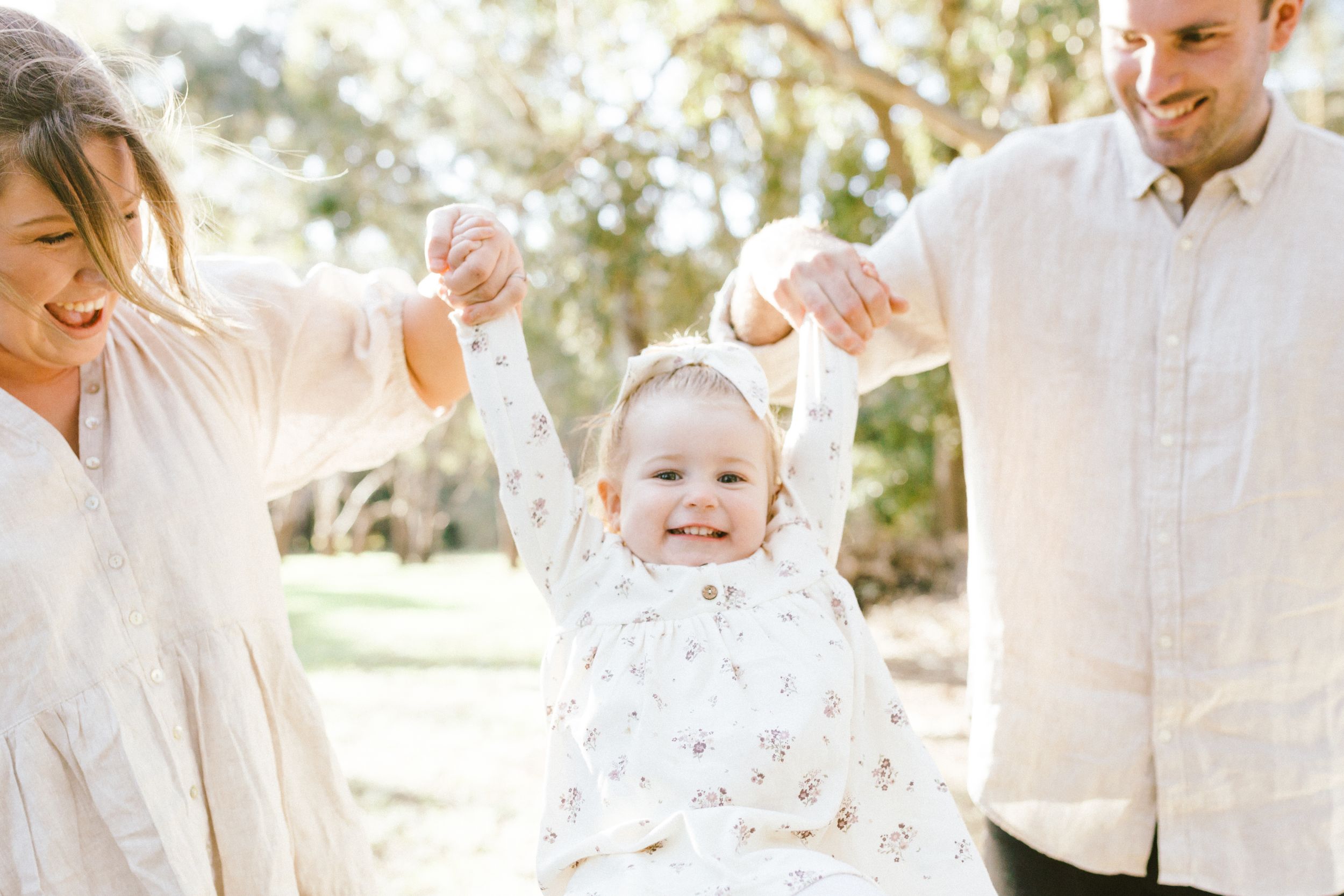 A family wearing white outfits poses together in a sun-drenched outdoor setting for a portrait session.