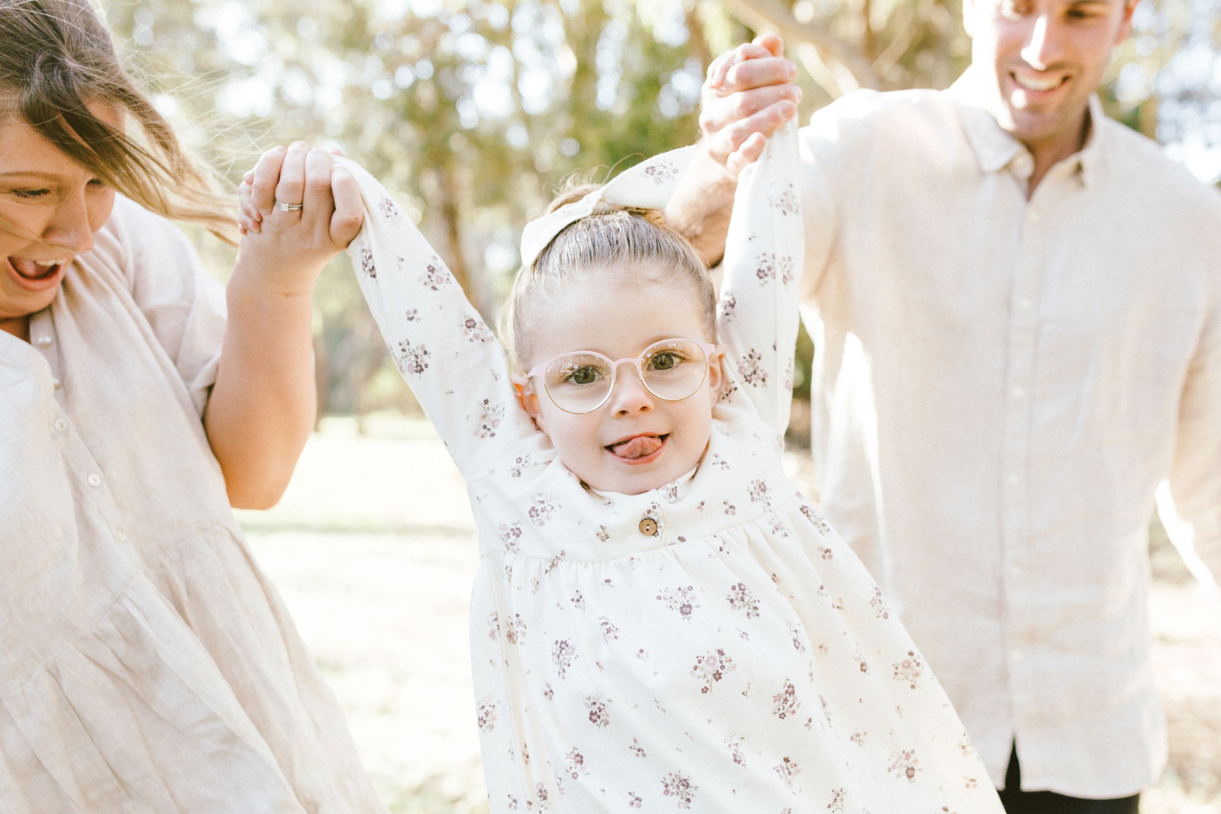 A happy family in white shirts plays together outdoors in the bright sunlight.