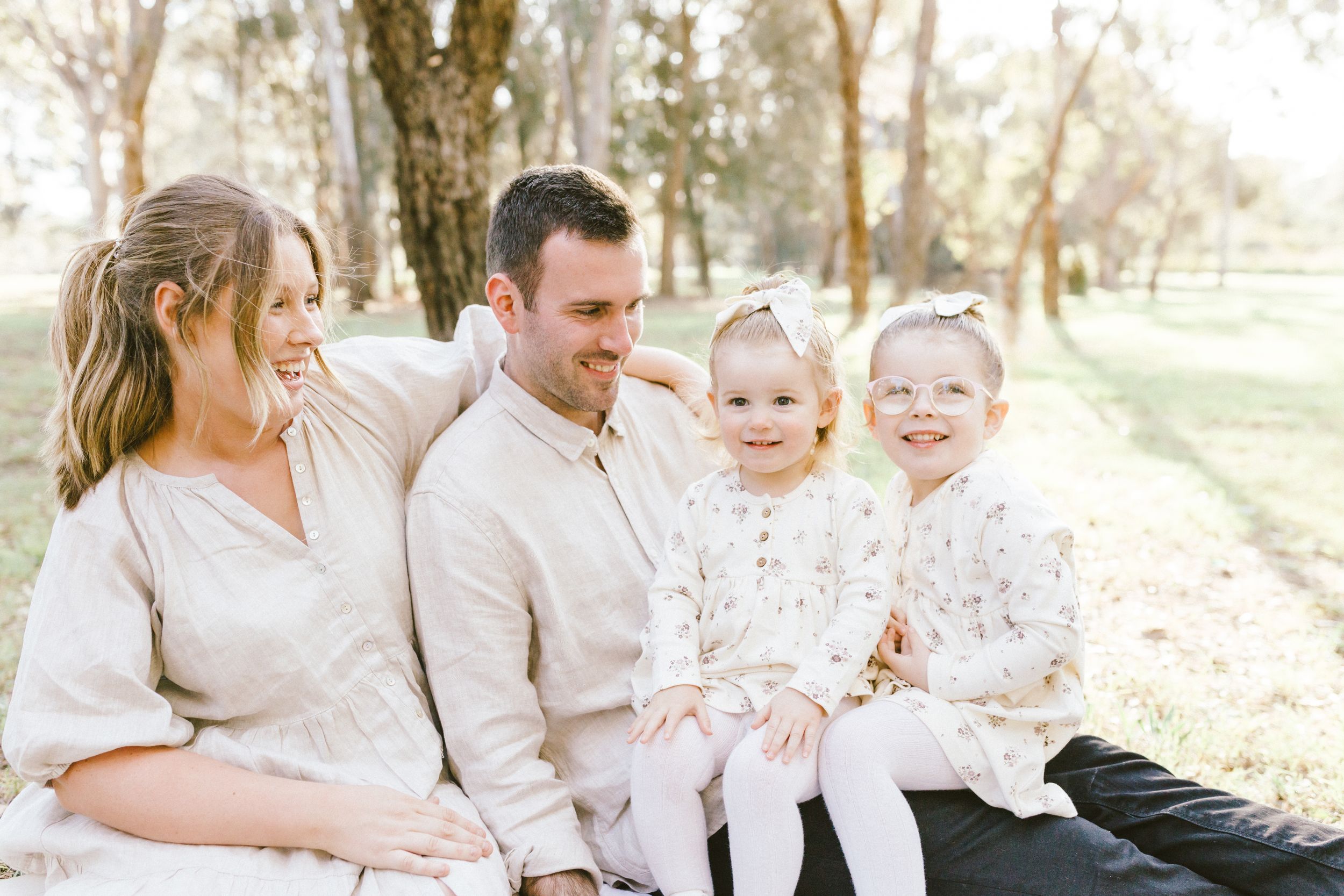 A joyful family wearing coordinated white outfits poses together in a sunlit outdoor setting during golden hour.