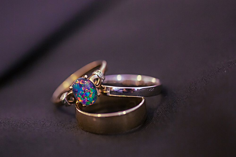 Close-up view of gold wedding rings with opal stone accent against dark background.