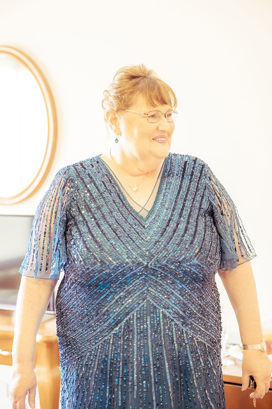 Person in a sparkling navy blue V-neck dress with short sleeves stands in an interior setting with white walls.