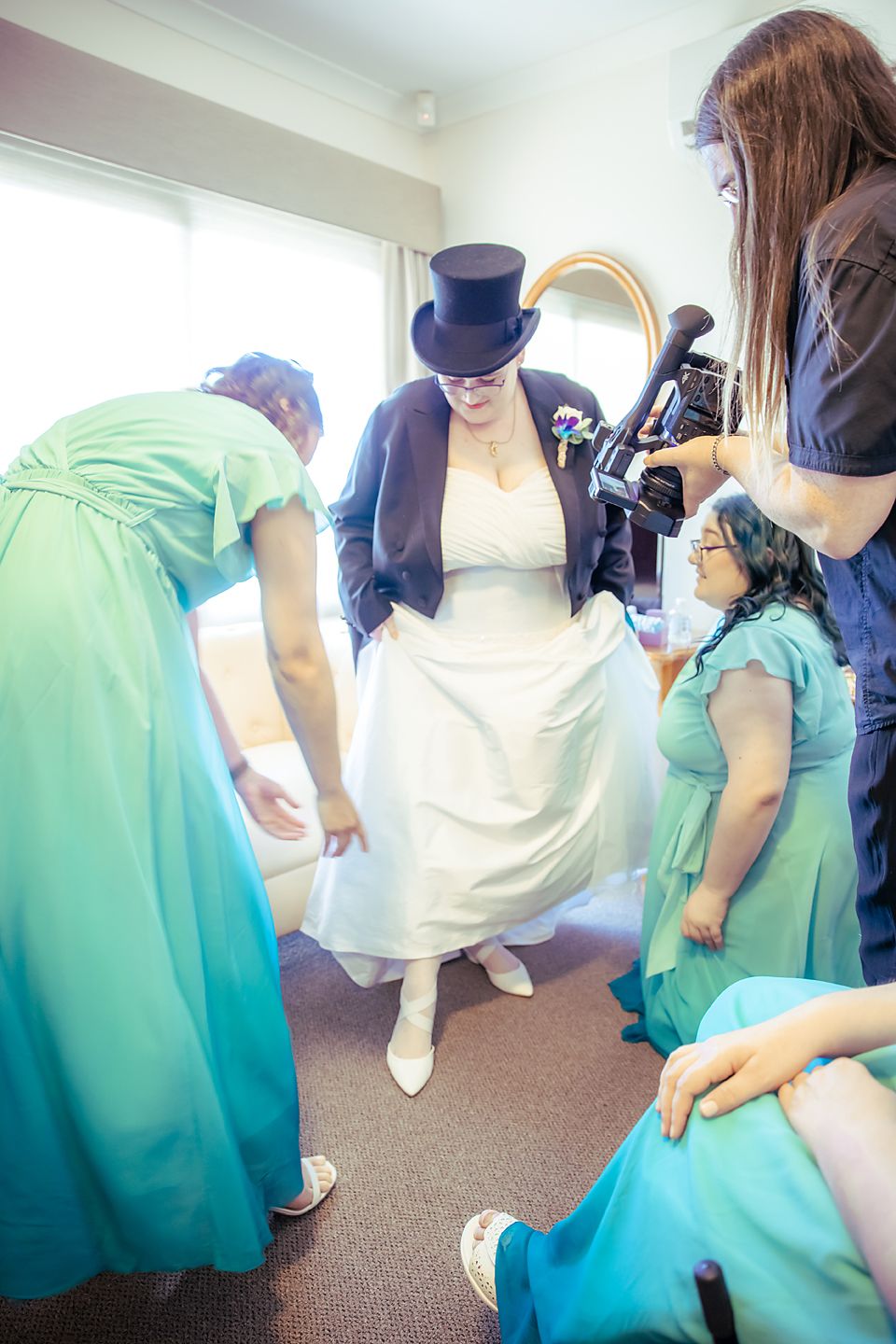 Wedding party helps adjust aqua blue bridesmaids dresses while preparing for formal photos at a celebration.