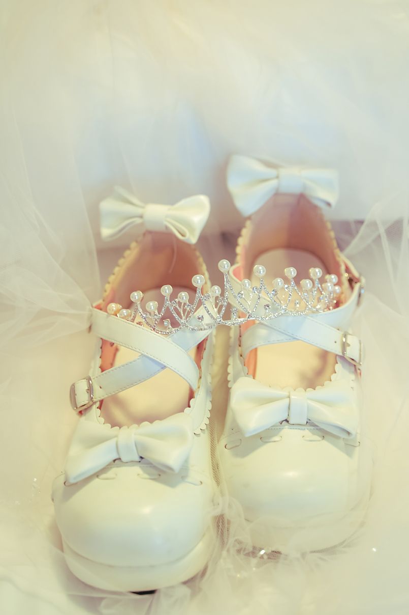 Vintage white baby shoes adorned with delicate bows and tiny crystal crowns create a dreamy, ethereal composition.