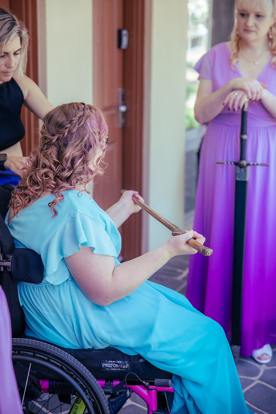 A person in turquoise dress in a wheelchair dances alongside others wearing purple dresses at a formal event.