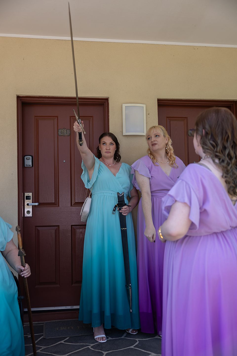 Bridesmaids wearing turquoise and purple dresses pose together in front of a wooden door at a wedding venue.