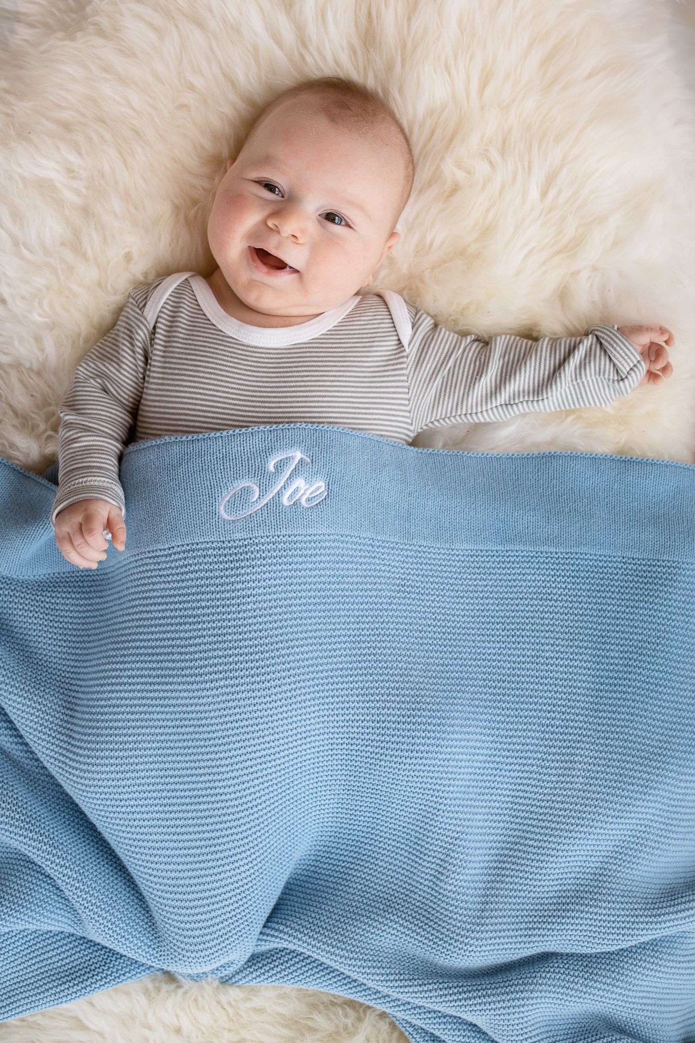 Newborn baby boy lying down smiling at the camera wrapped in a  blue blanket.