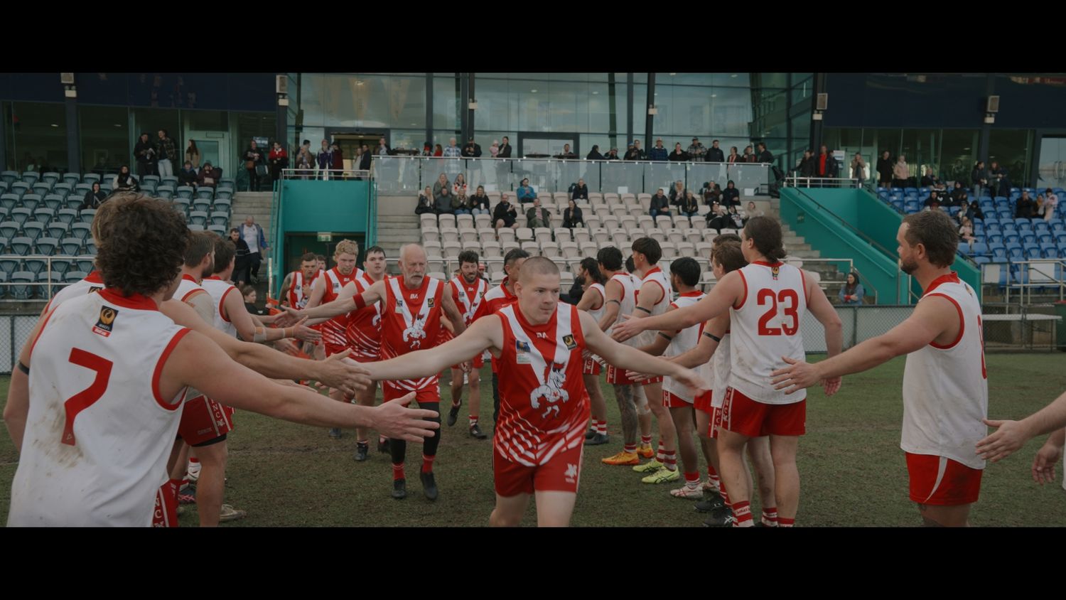 Athletes in red and white uniforms form a celebratory tunnel on a sports field after a game.