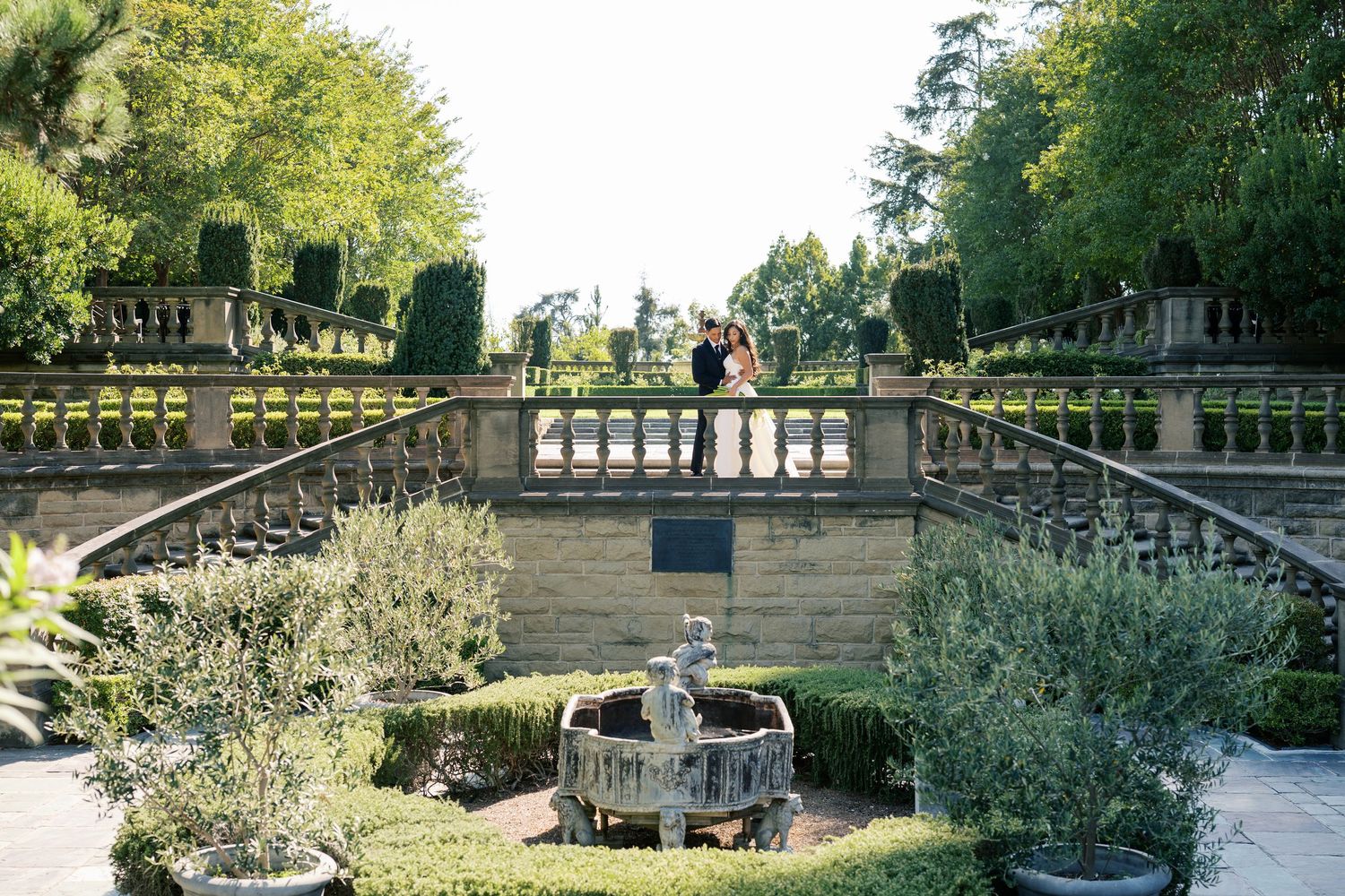 A panoramic view of a landscaped garden terrace with stone balustrades and mature trees in the background.