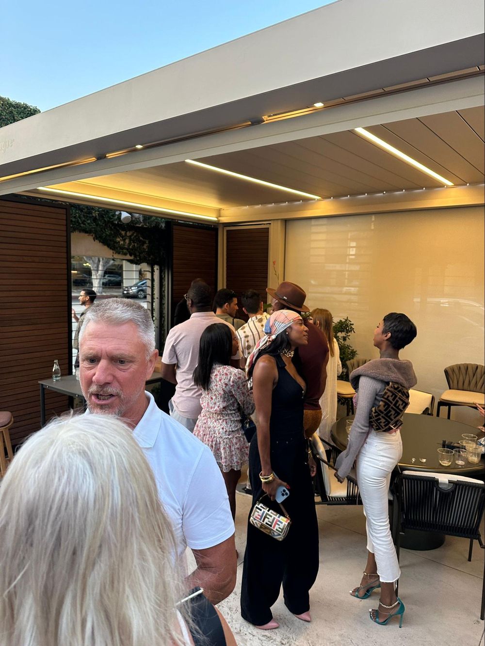 A group of people gathered under a modern outdoor covered patio with warm lighting during an evening event.