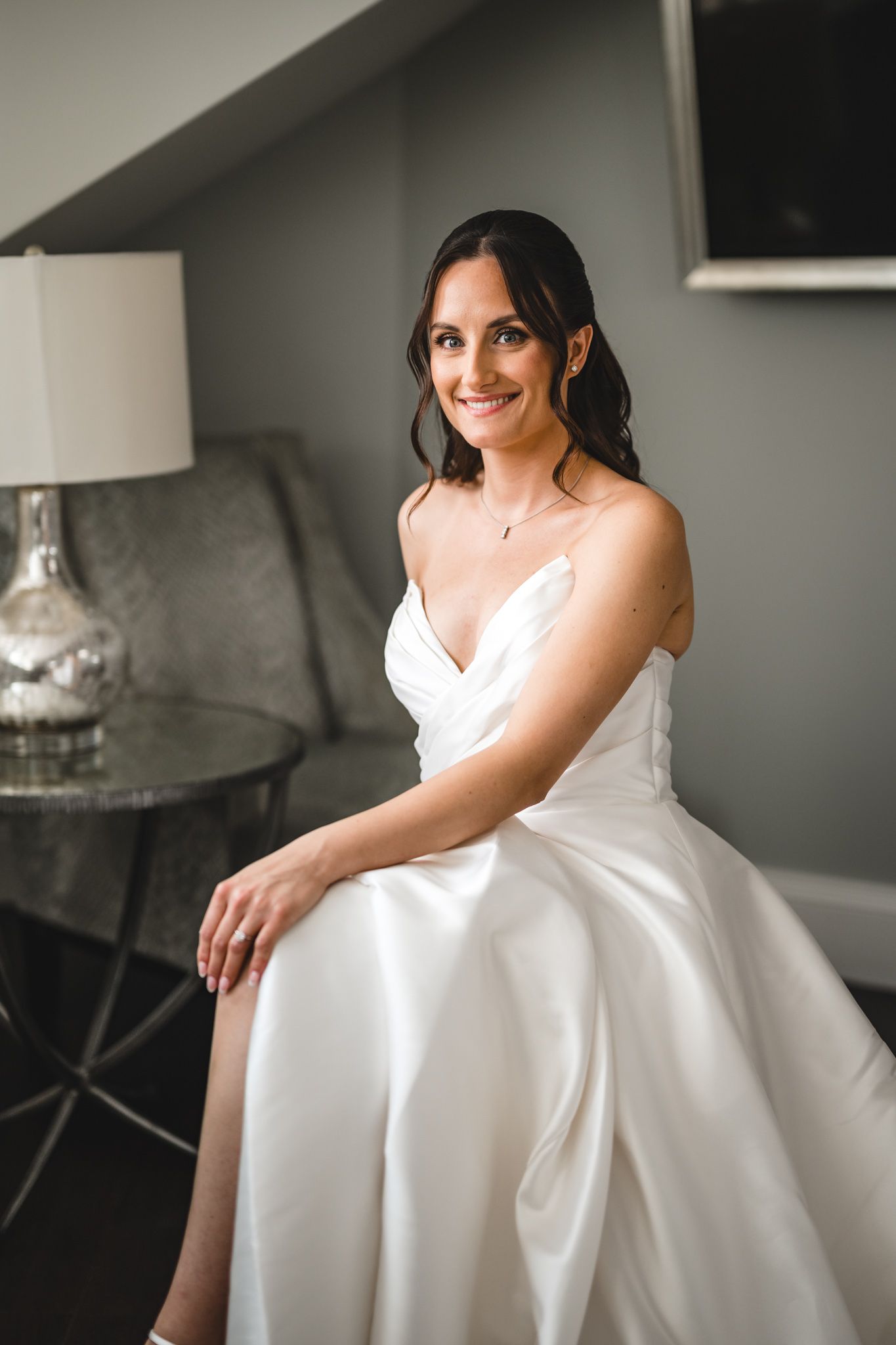 Bride in elegant white wedding gown sitting on couch for portraits.