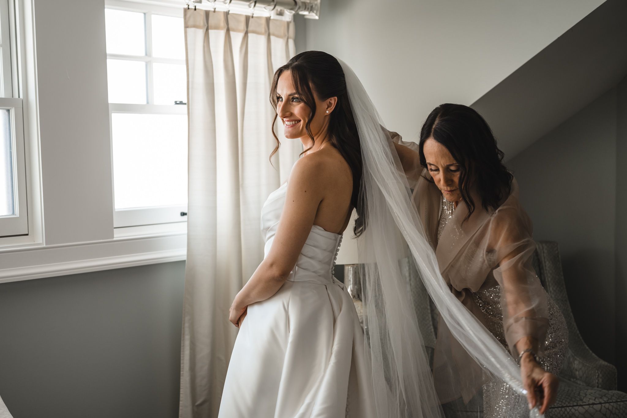 Elegant white wedding dress being fitted in a bright modern room with natural lighting.