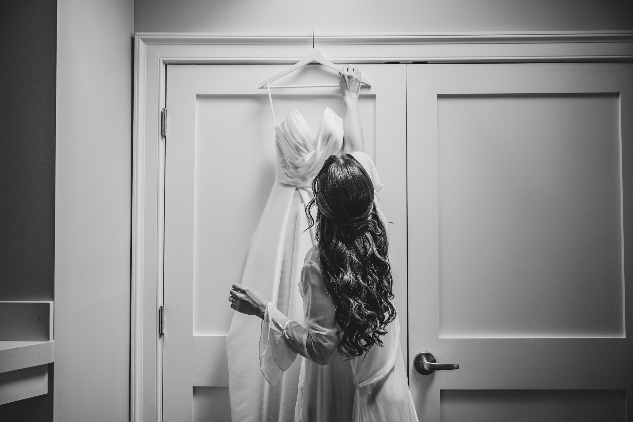 Black and white image of a bride getting ready in an elegant white wedding dress.