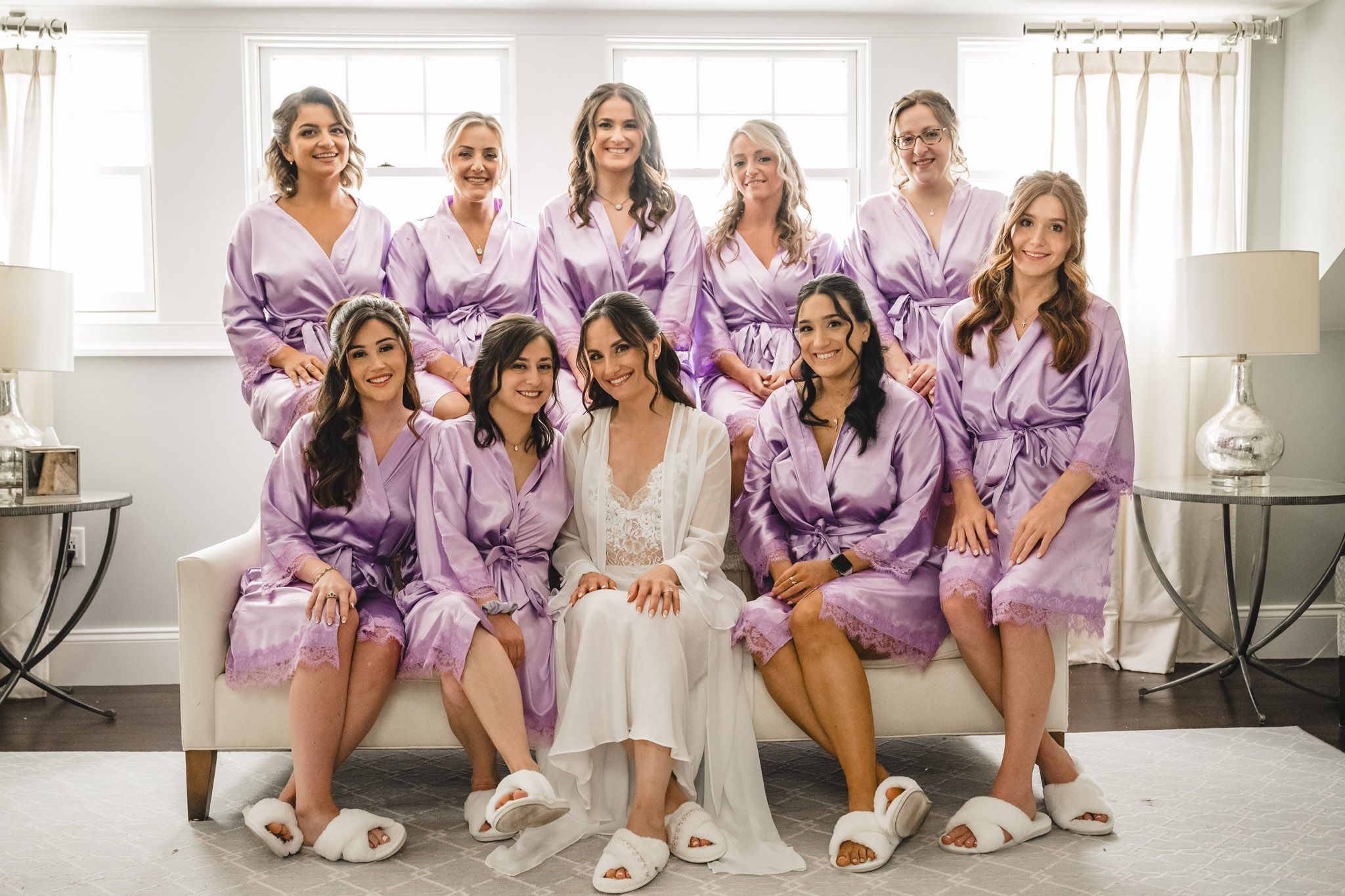Bridesmaids in lavender robes sitting together on floor during wedding preparations.