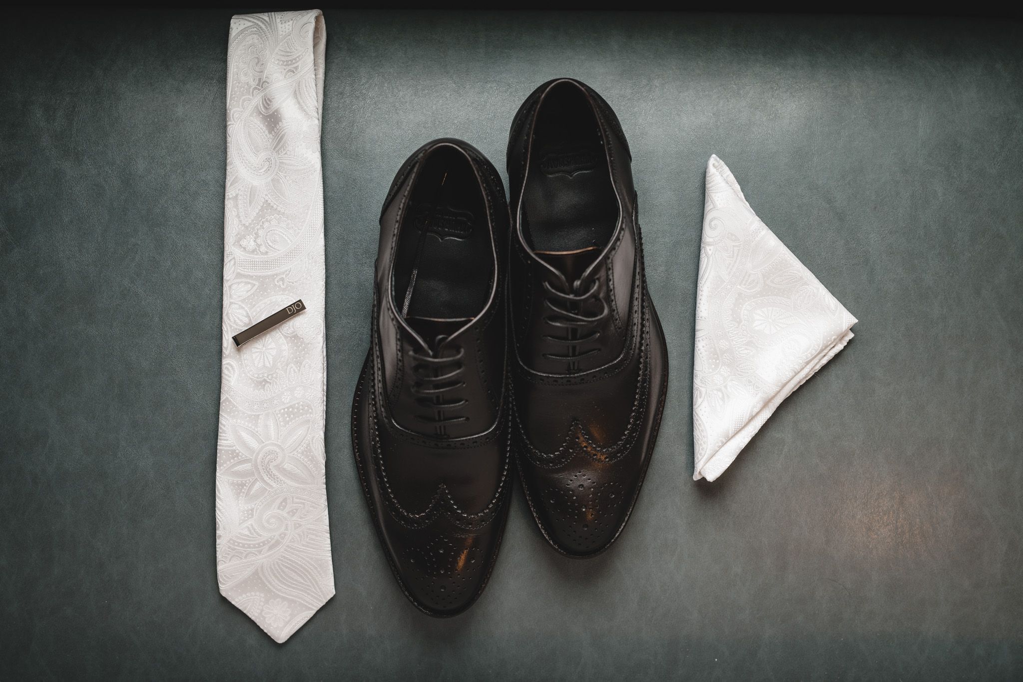 Wedding accessories including dress shoes and tie arranged on dark background.