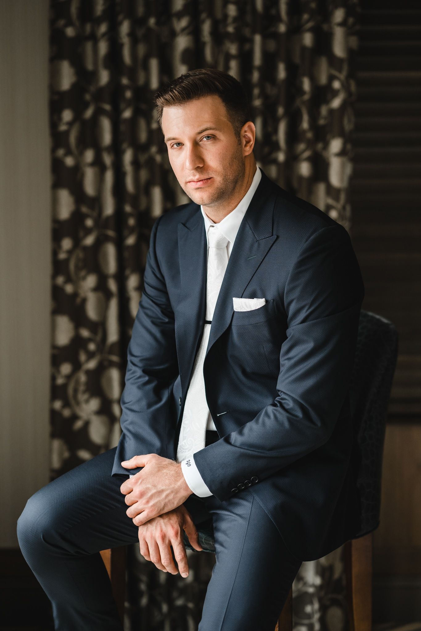 Professional portrait session showing details of a navy suit and white tie in an elegant indoor setting.