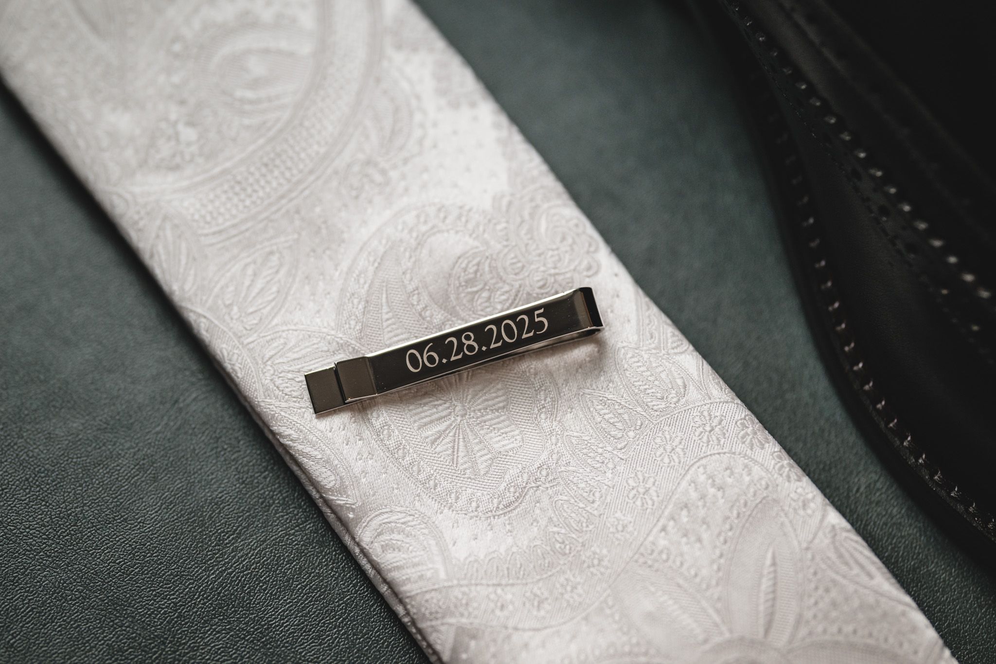 Close-up of formal white tie and accessories against dark textured surface.