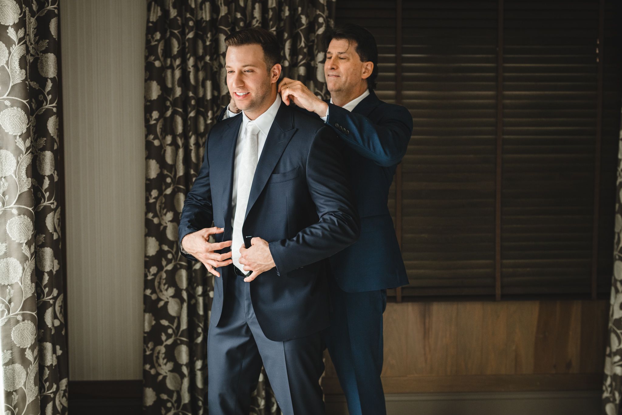 Wedding party members in dark suits laughing together during pre-ceremony preparations.
