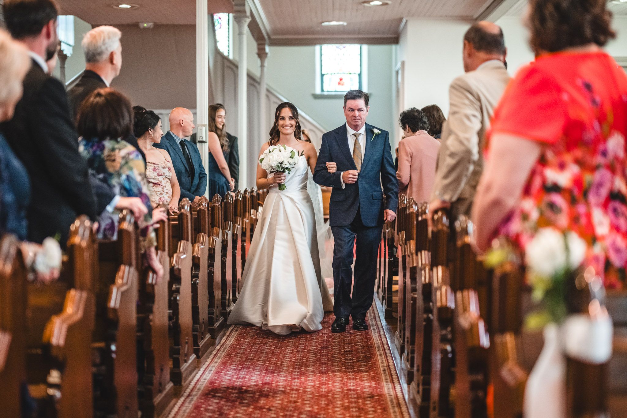 Wedding ceremony processional in church with red carpet and wooden pews.
