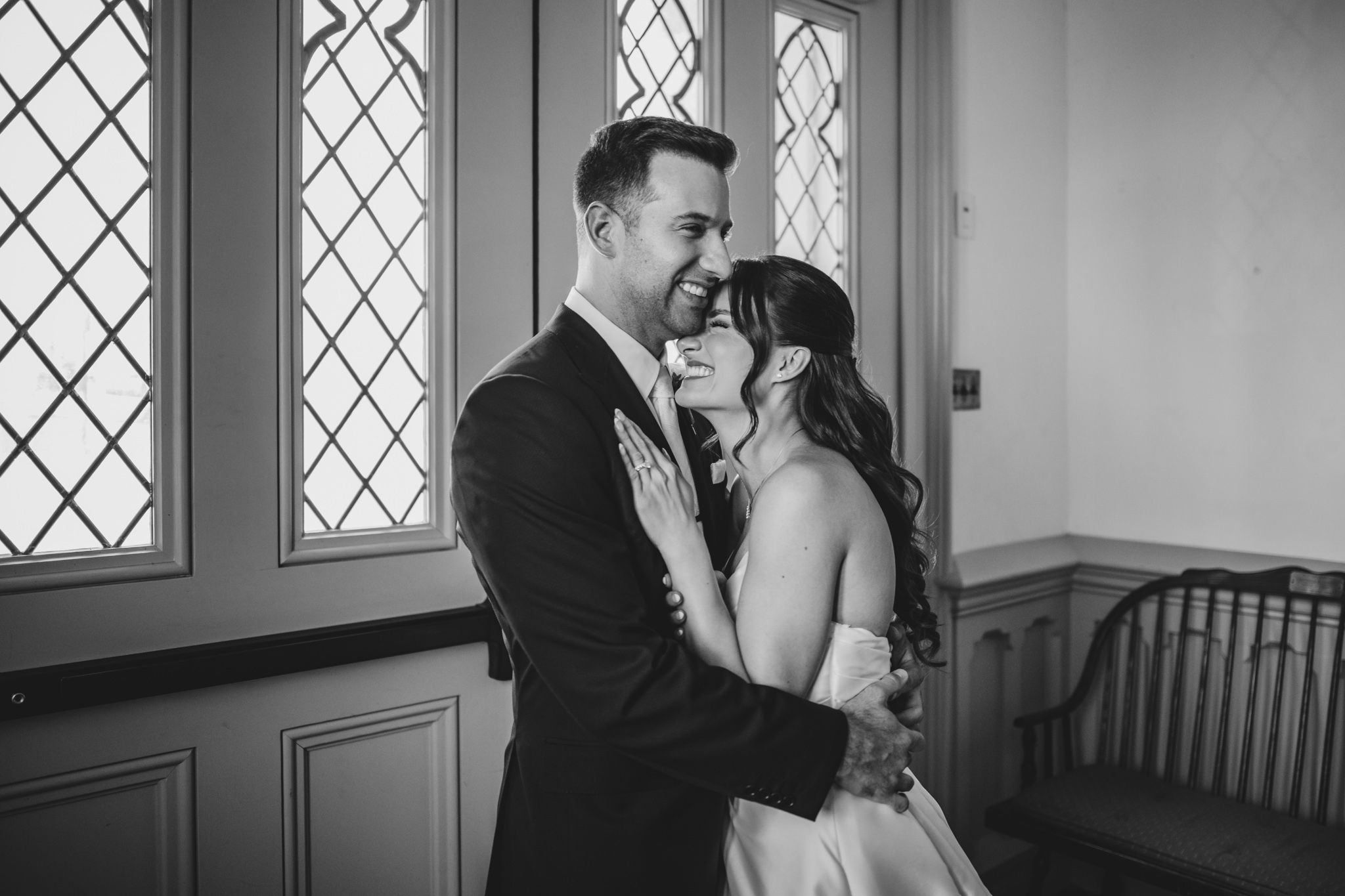 Intimate wedding moment captured by diamond-paned windows in black and white.
