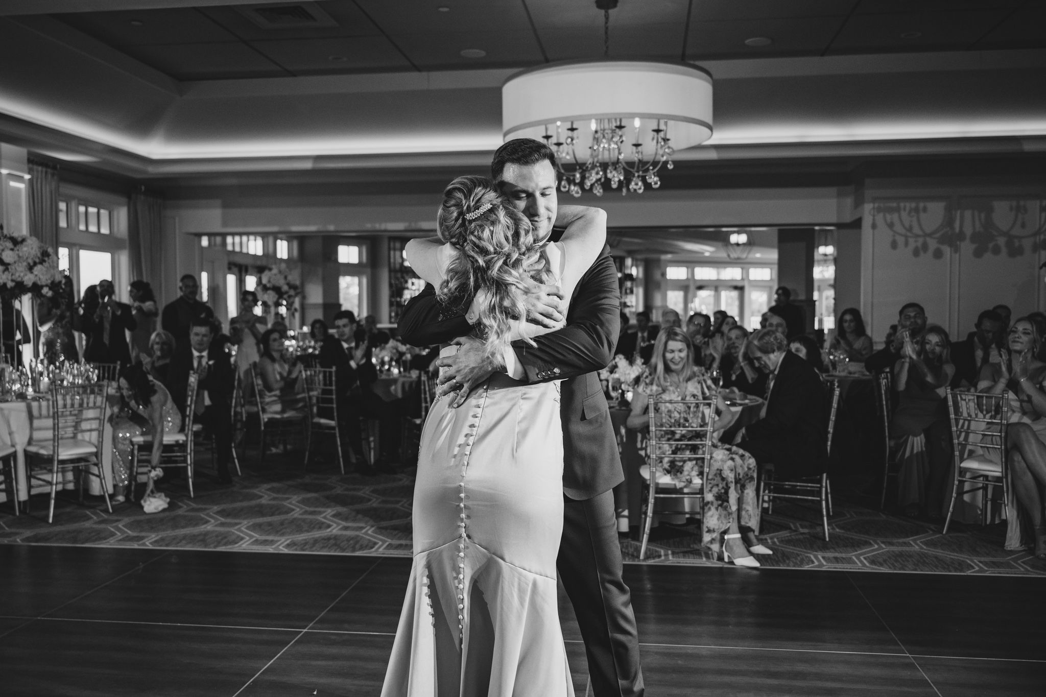 Black and white image of elegant dance performance in chandelier-lit ballroom setting.