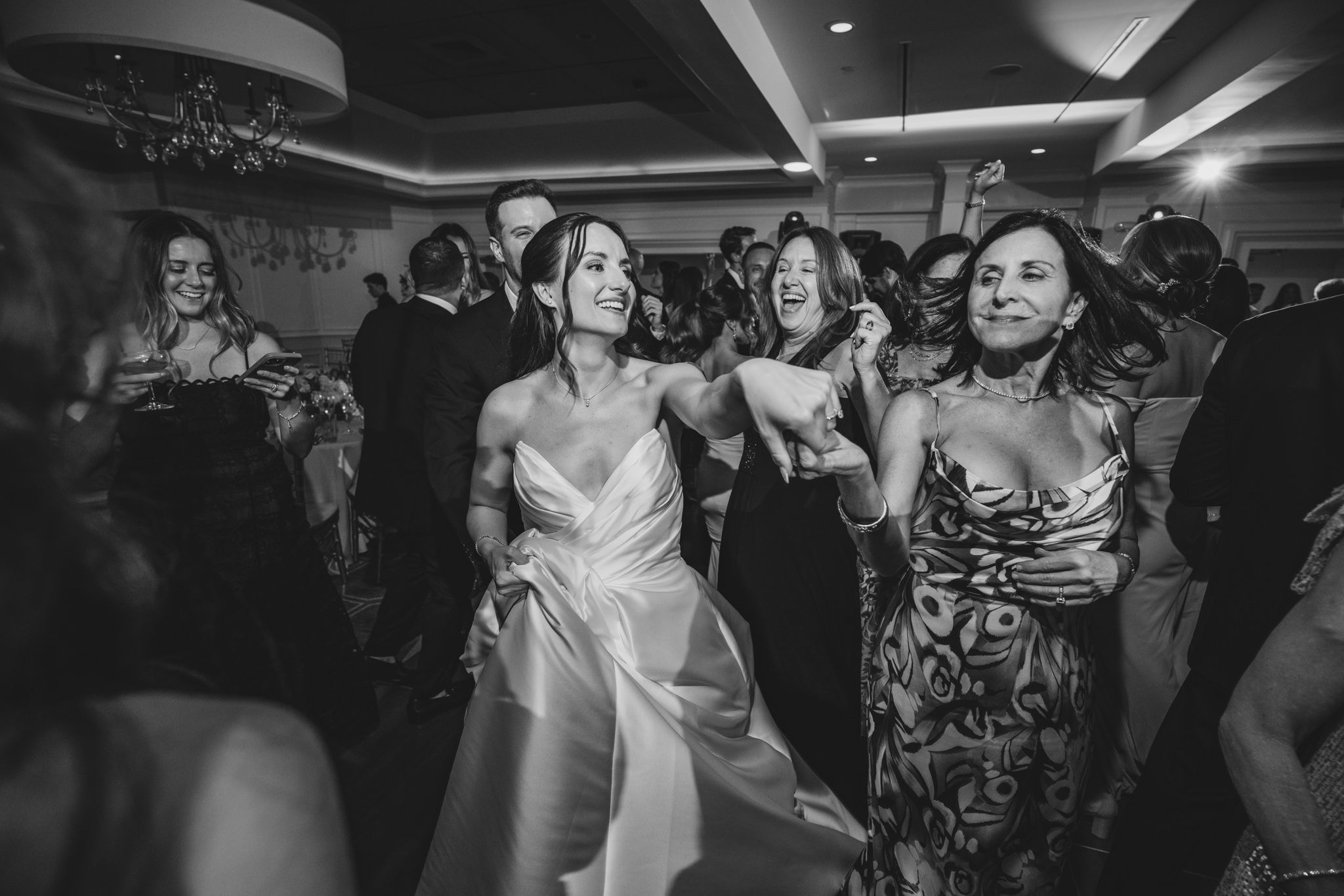 Wedding party guests dancing and socializing under modern ceiling lighting.