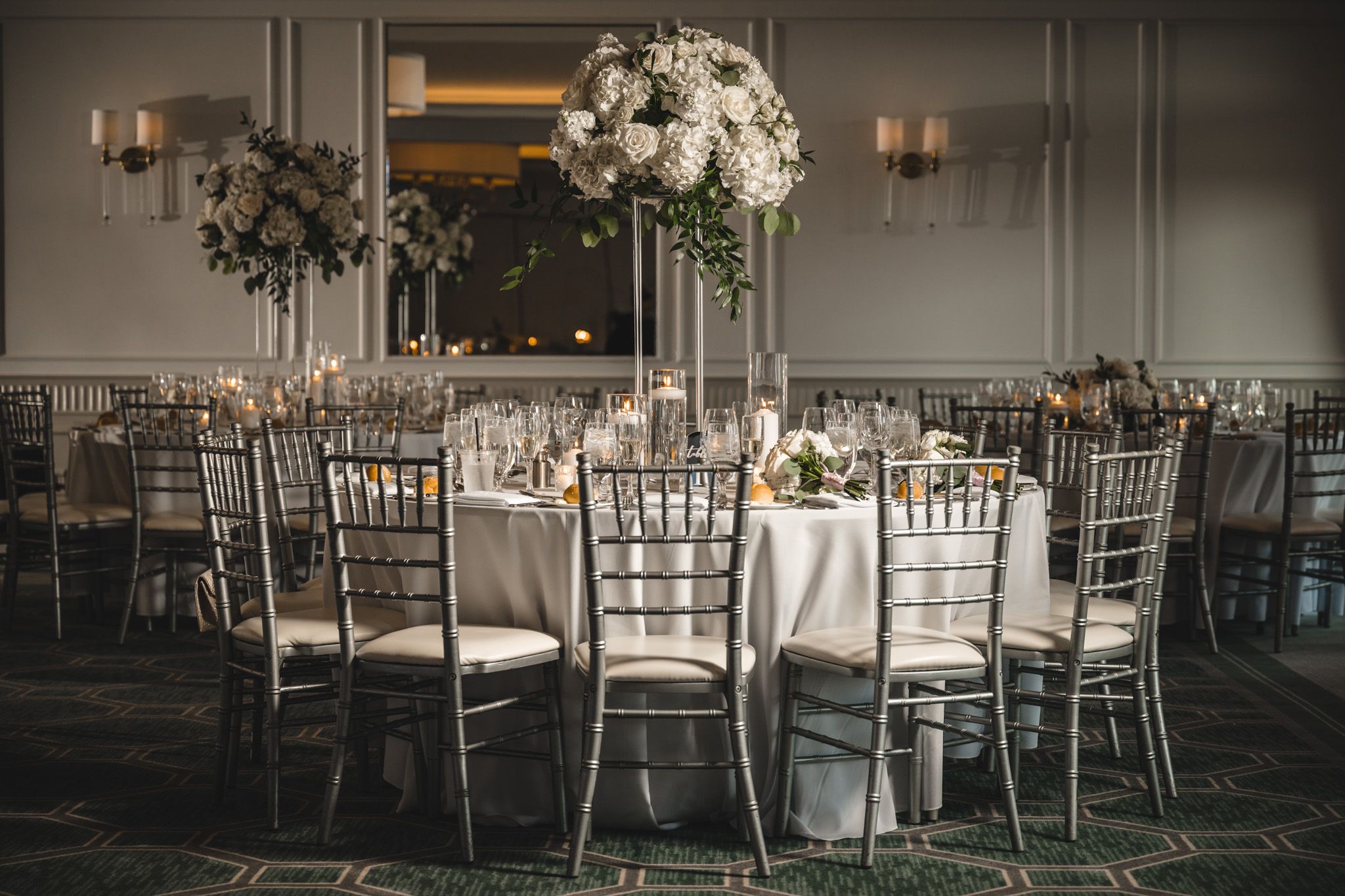 Wedding reception setup with white chiavari chairs and floral centerpieces.