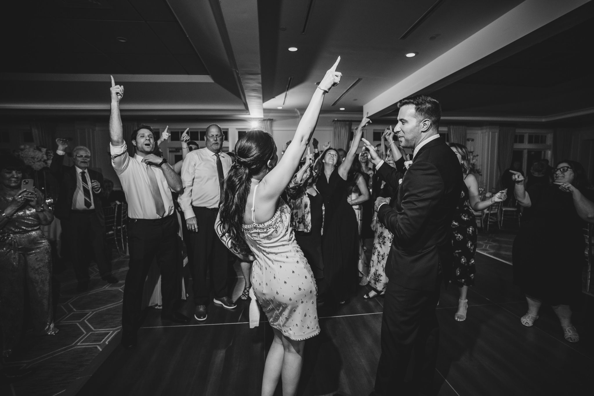 Black and white photo of wedding guests dancing and celebrating at a reception.