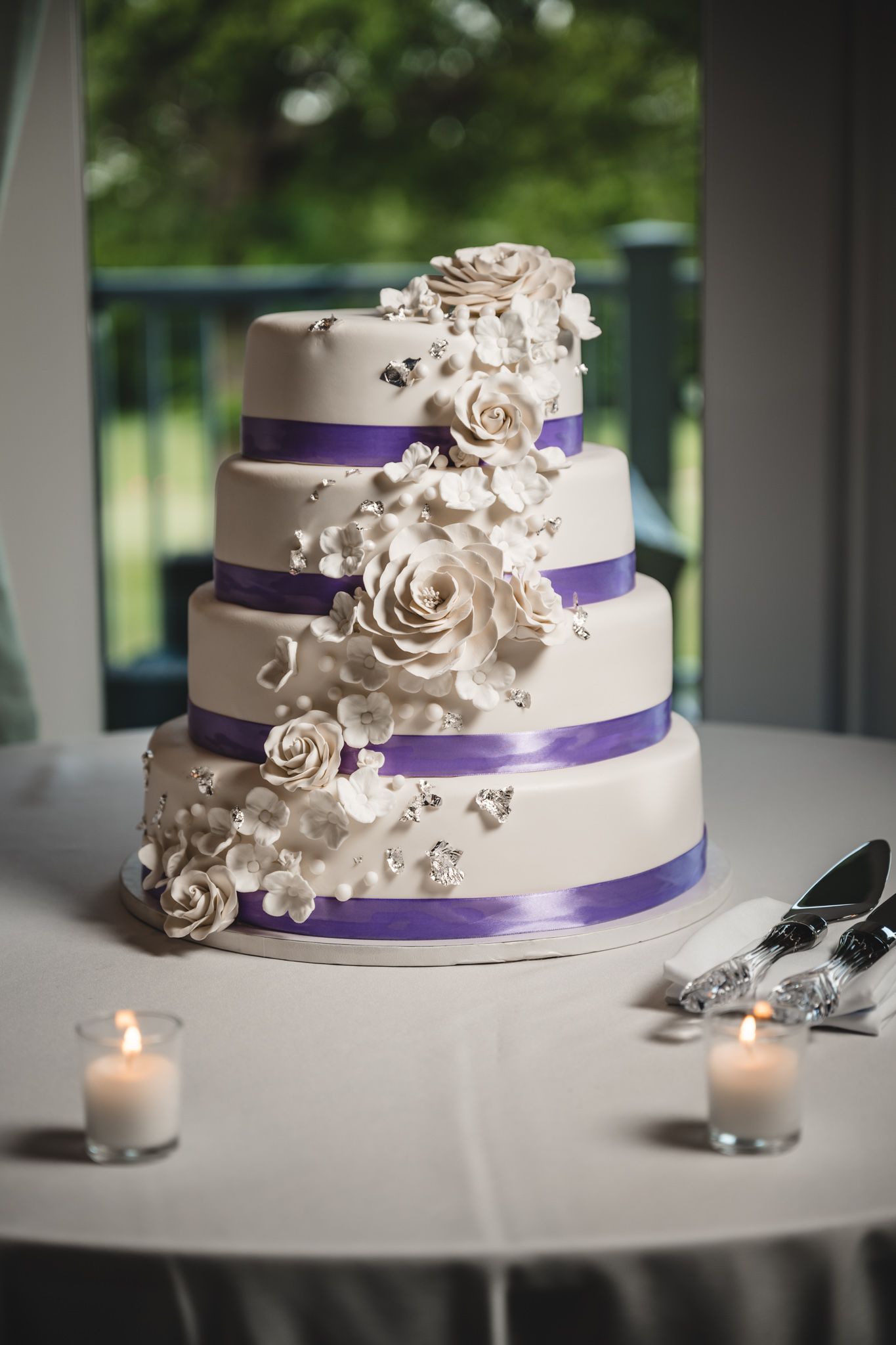 White wedding cake with purple ribbon and cascading sugar flowers.