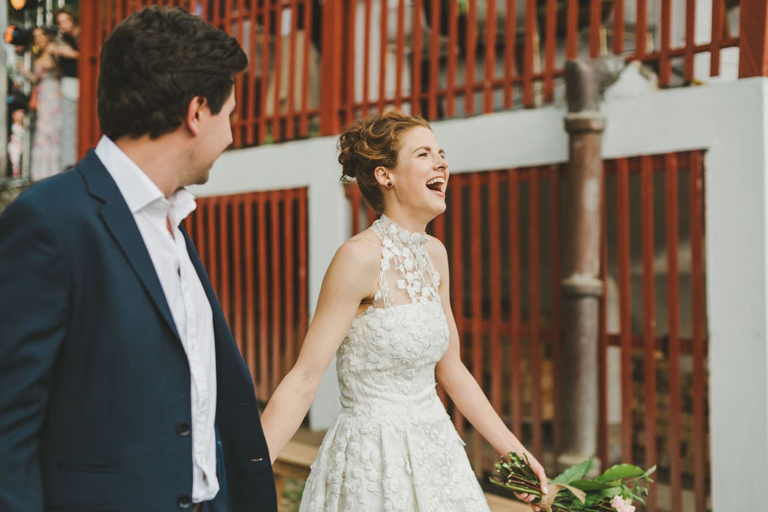 Couple shares candid laughter during outdoor photo session with rustic wooden backdrop.