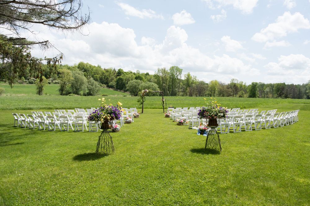 White chairs and flower arrangements line both sides of a grassy outdoor wedding ceremony space in spring.