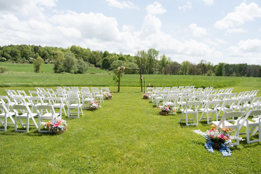 White chairs set up on green grass lawn for outdoor wedding ceremony with scenic rolling hills in background.