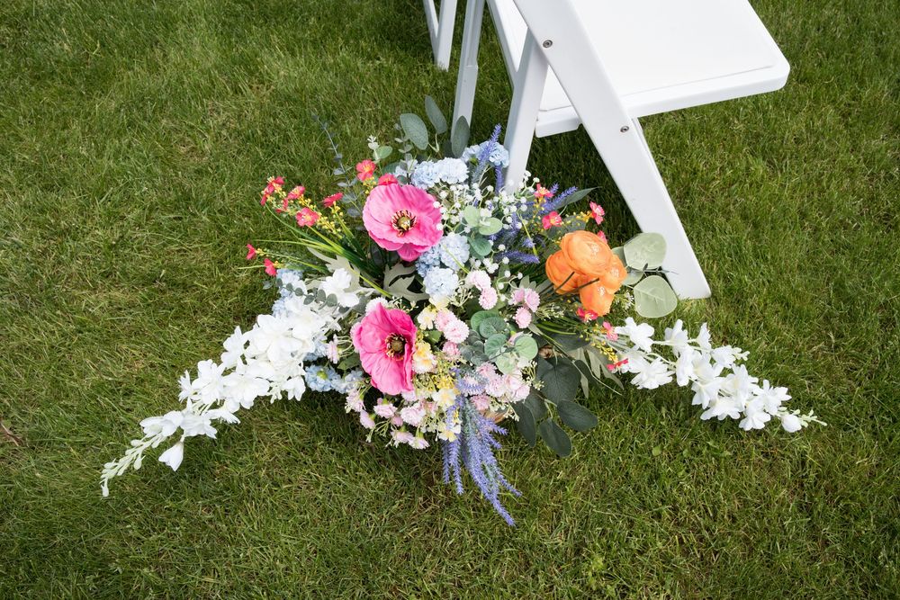 Multiple small white crosses decorated with colorful floral arrangements lay scattered on green grass.