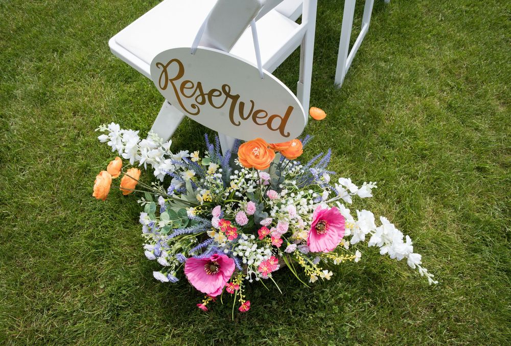 Rustic white chairs with floral decorations arranged for an outdoor wedding ceremony on a green lawn.