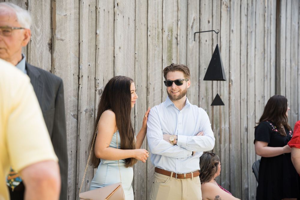 A group of people standing and mingling together at an outdoor event next to a wooden fence.
