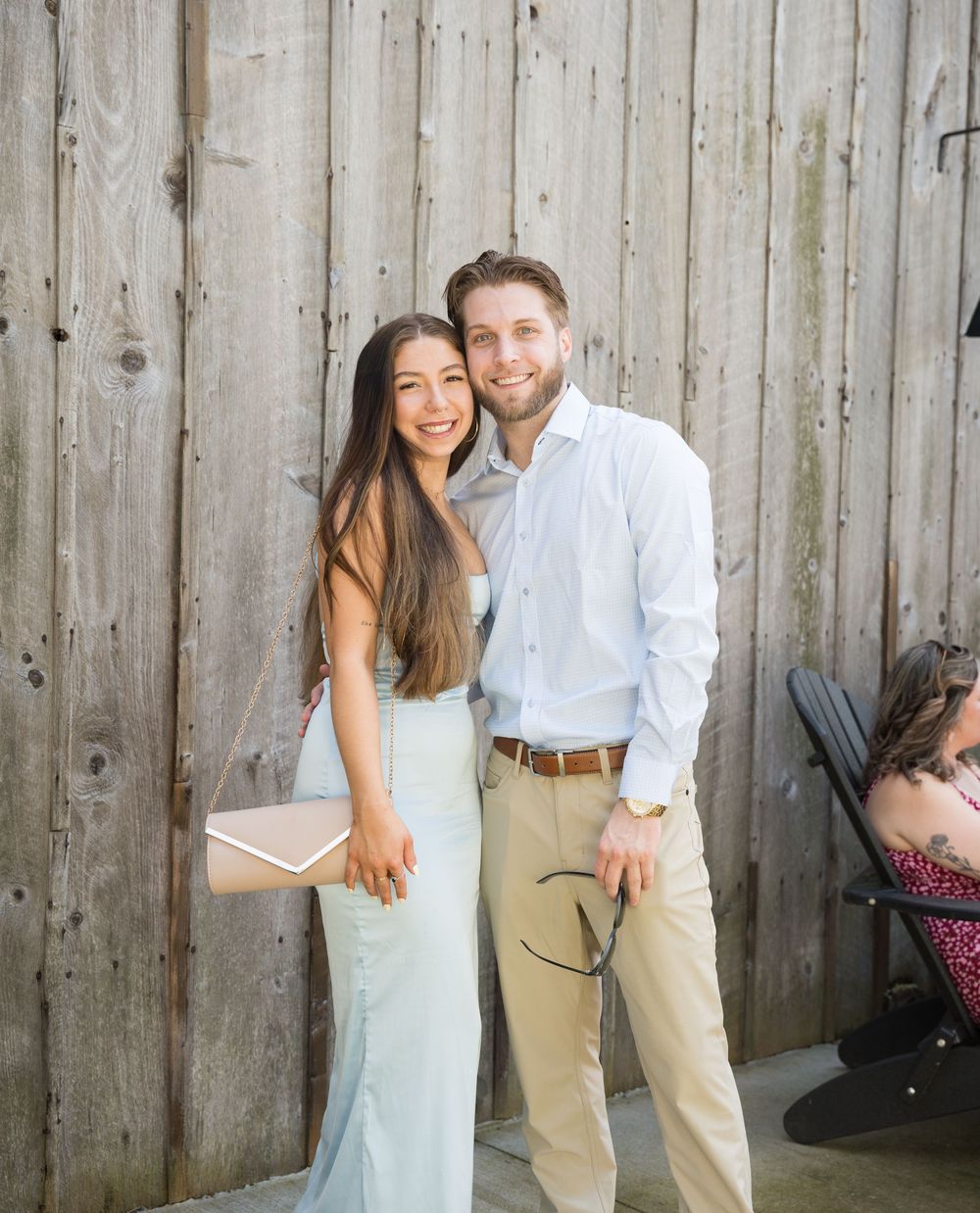 A smiling couple poses together outdoors against a rustic wooden fence during a photo shoot.