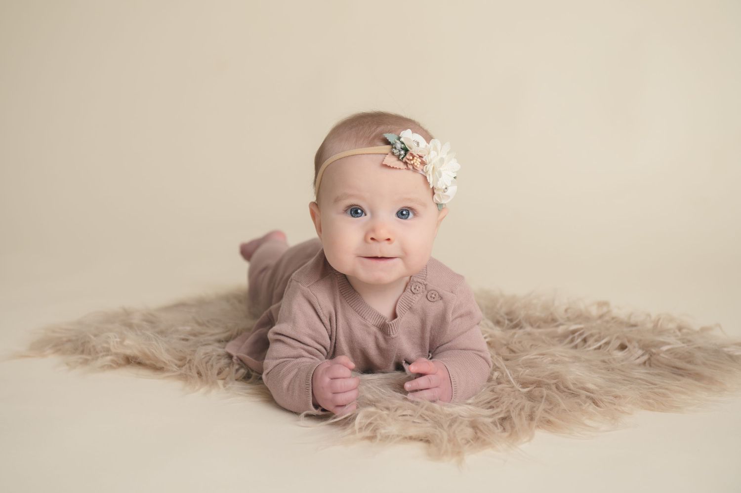 Baby portrait in soft neutral tones on cream backdrop with delicate headband.