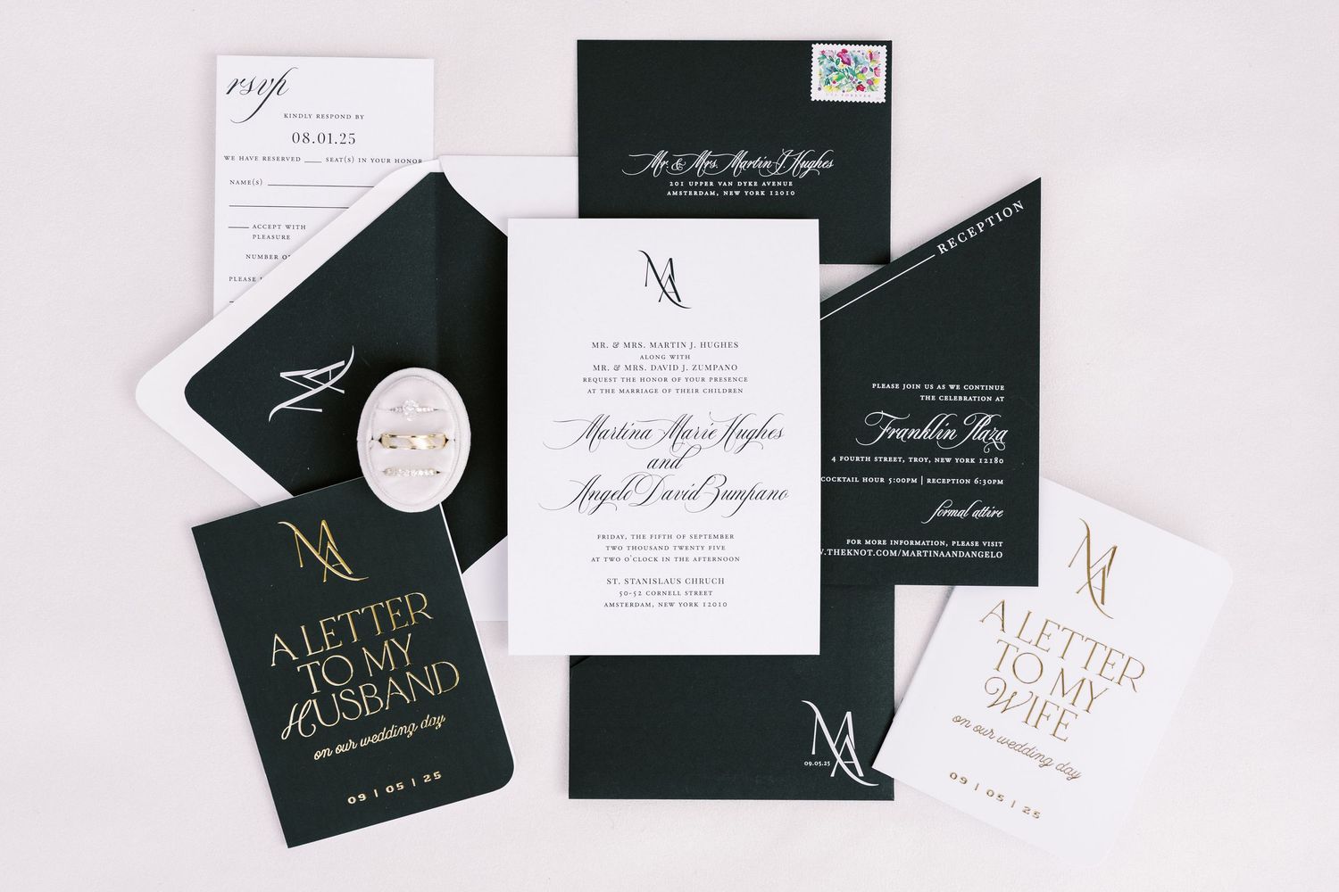 Elegant black and white wedding invitations with gold monogram details and matching envelopes arranged in a minimalist display.