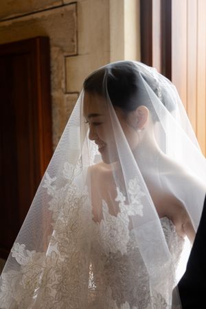 Elegant bride wearing traditional white lace veil in soft window light.