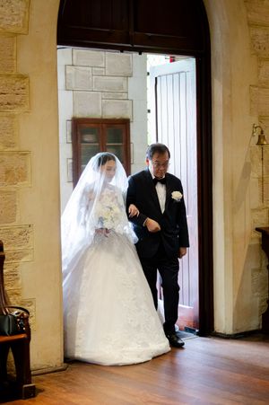 A wedding couple enters through an elegant stone archway with wooden doors.