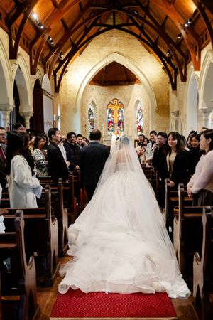 Wedding ceremony taking place in a beautiful Gothic church with exposed wooden beams and stained glass windows.