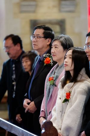 Wedding guests in formal attire seated watching ceremony in church.