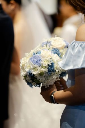 Bridal bouquet featuring blue and white roses held in soft lighting.