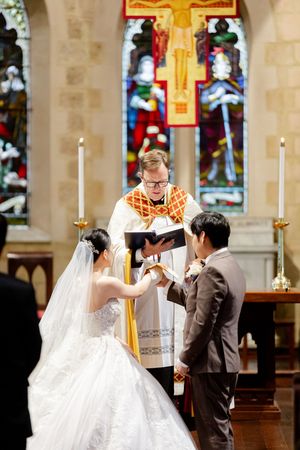 Wedding ceremony taking place in a traditional church with tall candles and stained glass windows.