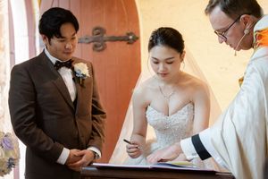 Wedding couple signing marriage documents with family members and officiant at registration table.